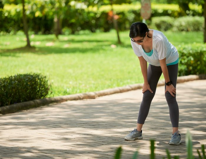 Portrait of adult Asian woman stopping to catch breath during jogging workout in park on sunny day